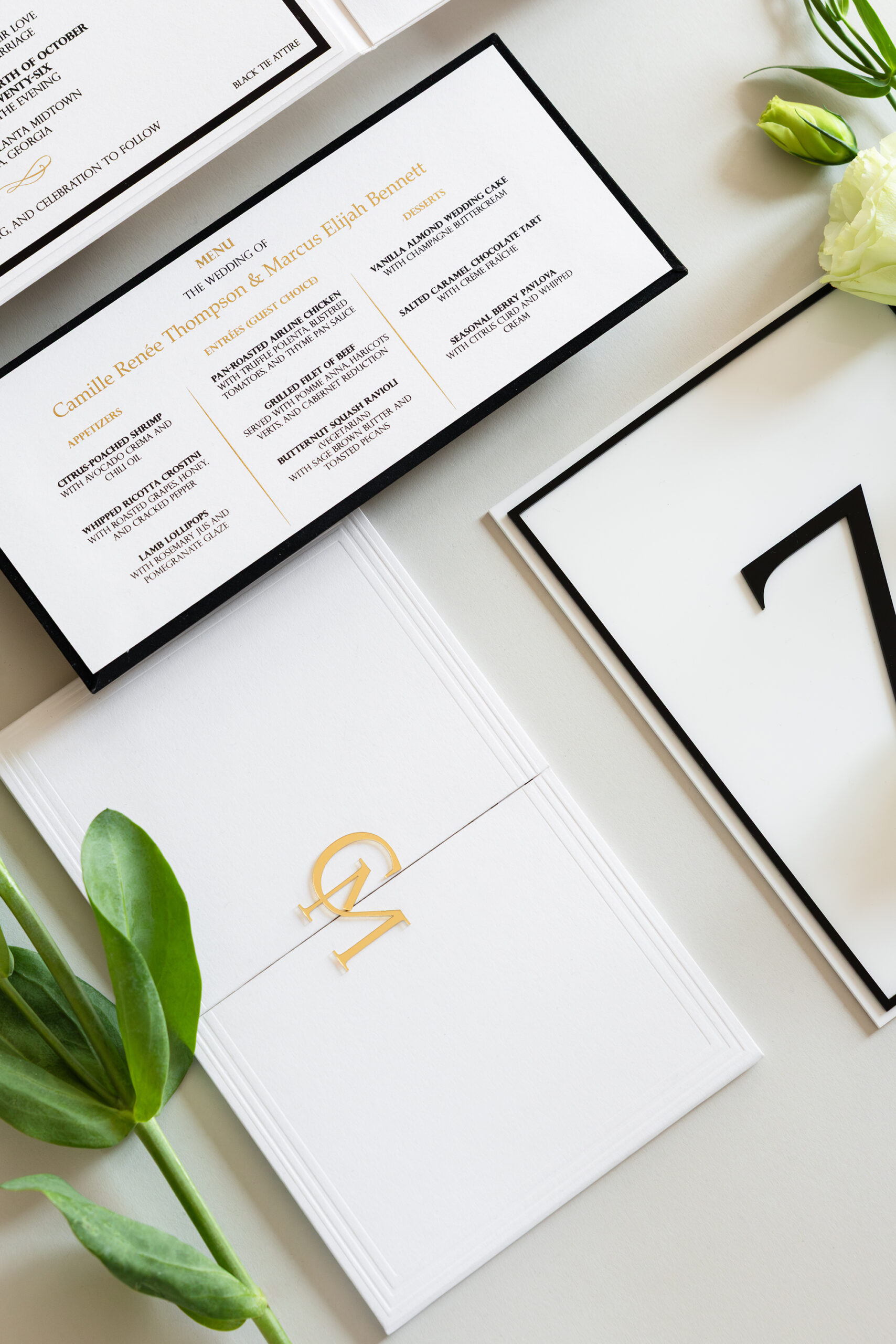 Luxury wedding menu card with gold foil typography, modern black border details, custom monogram, and coordinating table signage designed by Sherry Green Designs for planners and elegant wedding receptions