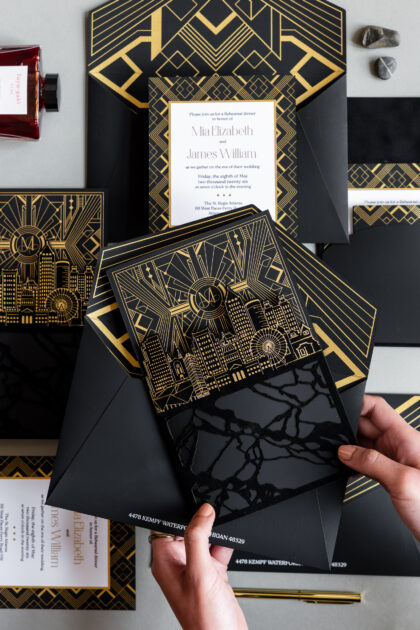 Luxury black and gold wedding invitation suite featuring gold foil Art Deco details, custom Atlanta skyline illustration, layered inserts, and glossy acrylic-inspired accents