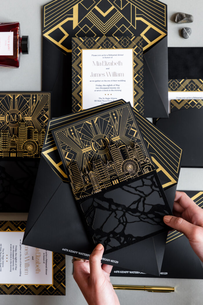 Luxury black and gold wedding invitation suite featuring gold foil Art Deco details, custom Atlanta skyline illustration, layered inserts, and glossy acrylic-inspired accents
