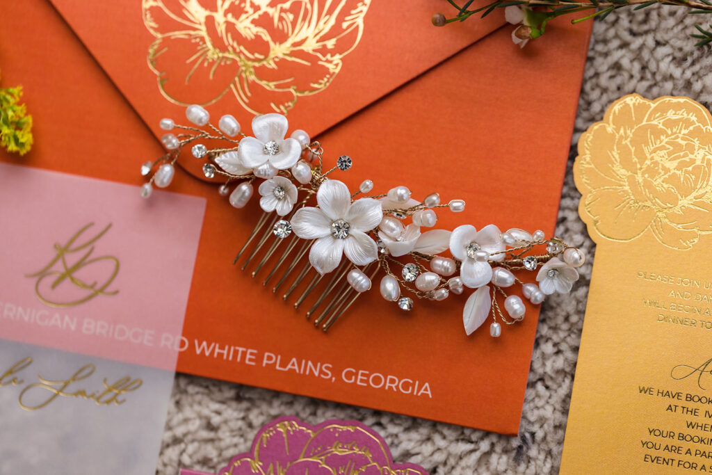 Luxury wedding stationery styling with vellum invitation, gold foil details, and floral hair accessory in pink and orange palette by Inked Green Designs
