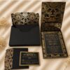 Luxury black and gold wedding invitation suite featuring an ornate floral presentation box, gold foil invitation, lace-inspired pocket, and coordinating RSVP card.