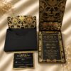 Luxury black and gold wedding invitation suite featuring an ornate floral pocket folder, coordinating presentation boxes, gold foil invitation, and matching RSVP card.