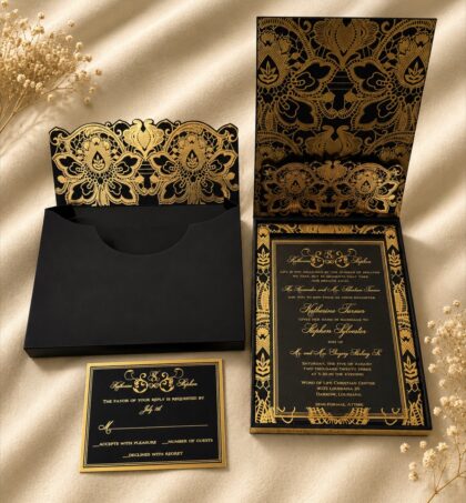 Luxury black and gold wedding invitation suite featuring an ornate floral pocket folder, coordinating presentation boxes, gold foil invitation, and matching RSVP card.