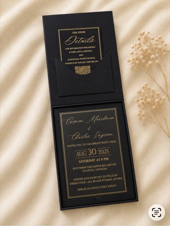 Luxury black wedding invitation box featuring a gold foil invitation card, matching details card in a black pocket, and premium presentation box displayed on an ivory fabric backdrop.