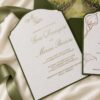 Custom vineyard wedding invitation featuring a watercolor venue liner, embossed white invitation with gold foil lettering, and coordinating RSVP card with calla lily illustrations in a deep green pocket envelope.